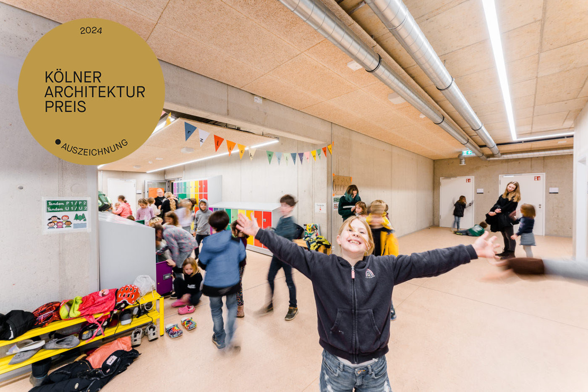 Ein fröhliches Kind mit ausgebreiteten Armen steht im Mittelpunkt eines geschäftigen Raumes voller Kinder.