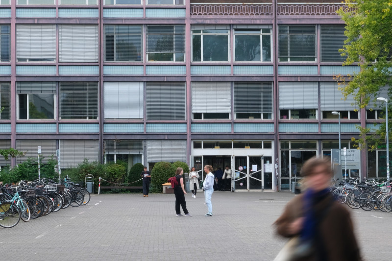 Moderne Gebäudeansicht mit Radabstellplätzen und Studierenden im Vordergrund.