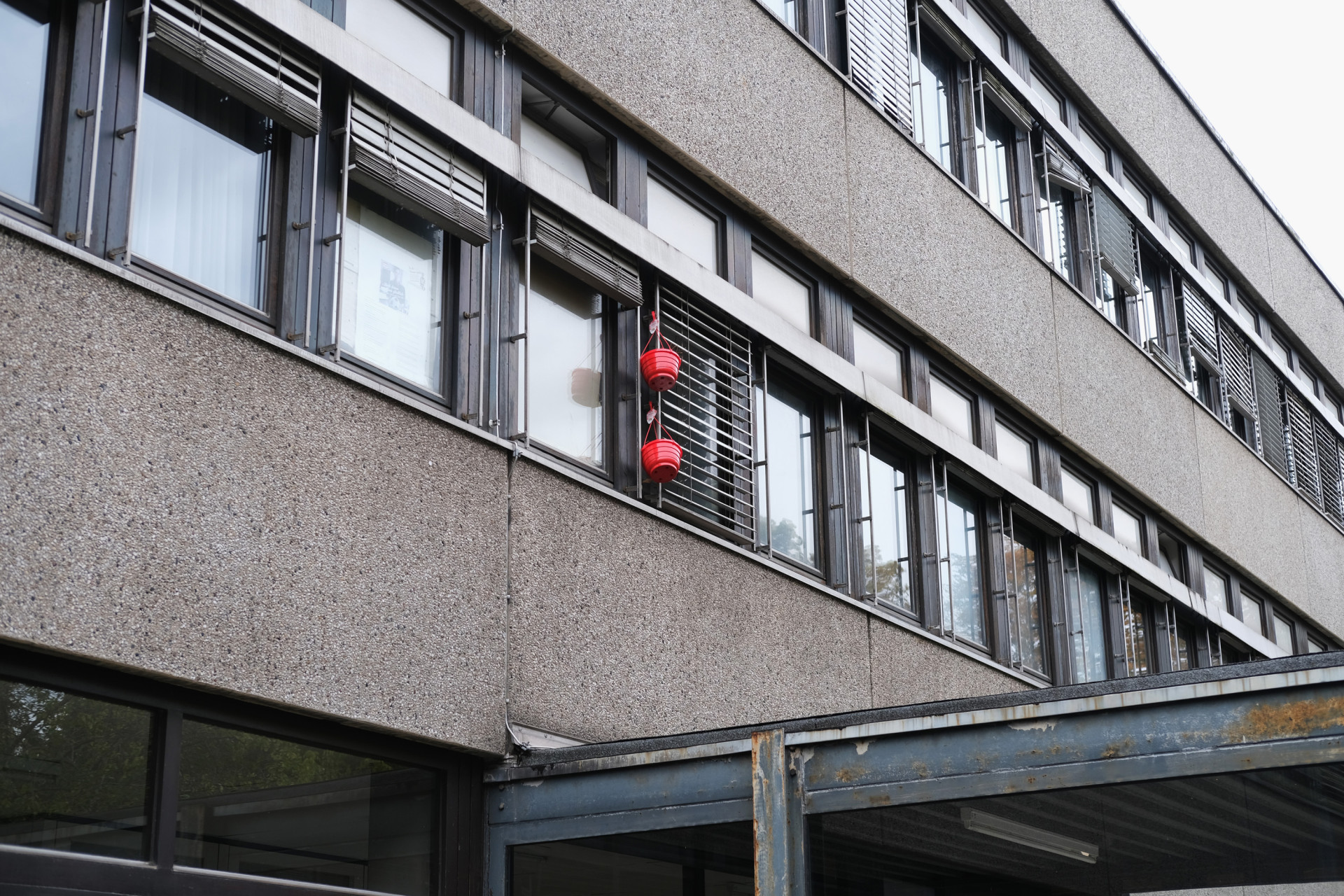 Blick auf ein graues Gebäude mit Fenstern und zwei roten Laternen im Vordergrund.