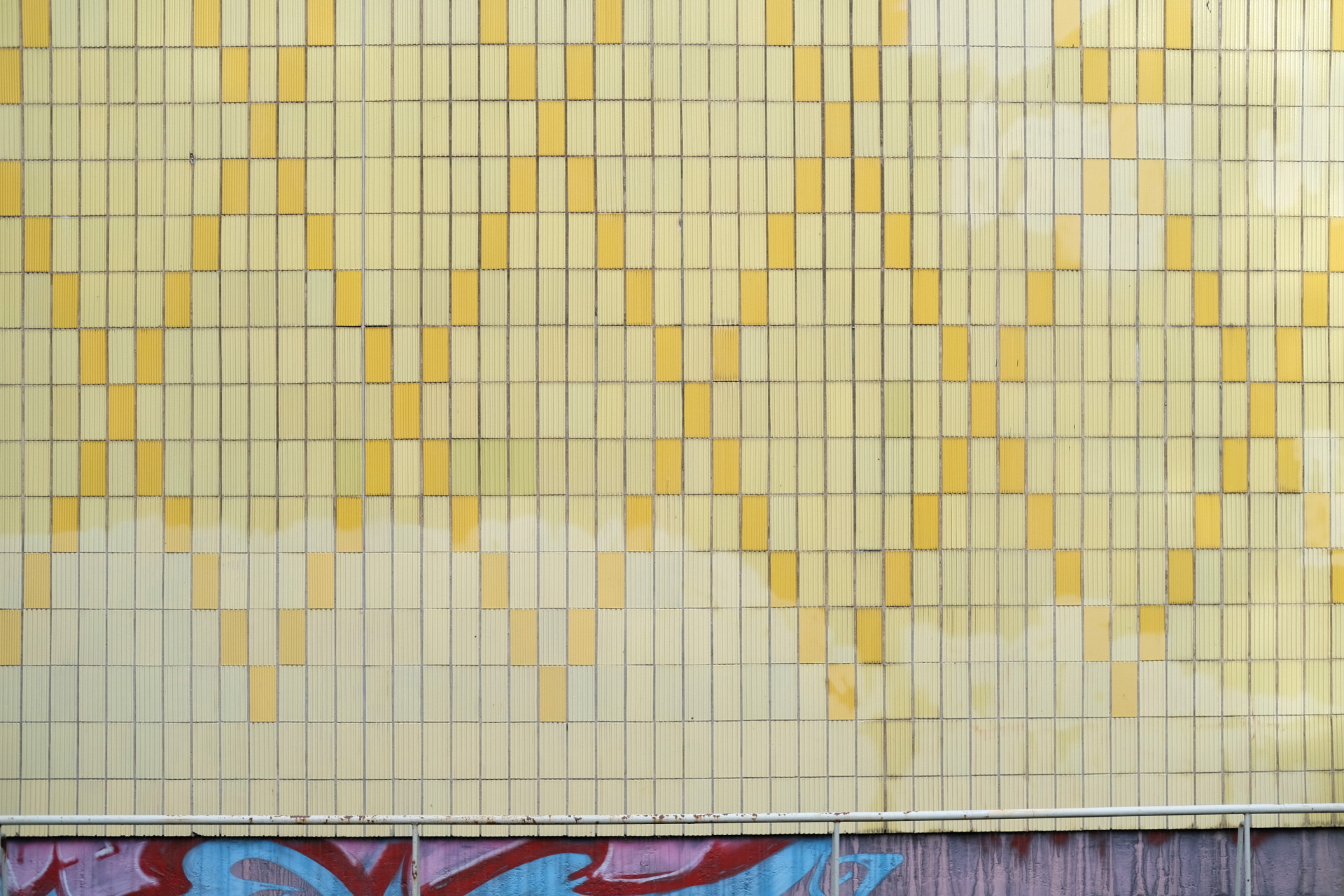 Gelbe Fliesenwand mit strukturierten Mustern und aufmerksamer Graffiti-Fundamentlinie.