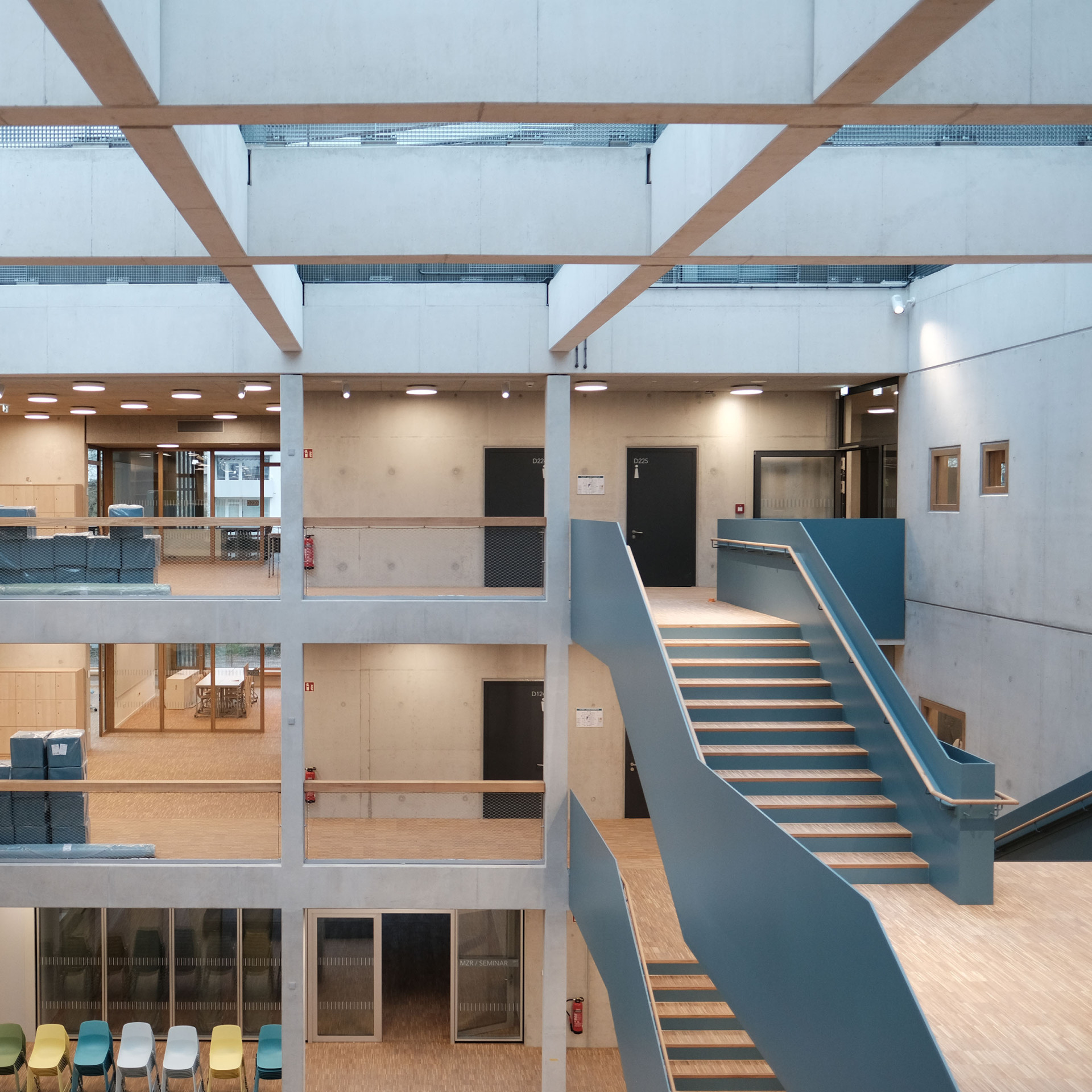 Innenansicht eines modernen Gebäudes mit offenen Etagen, Holztreppe und hellen Räumen.