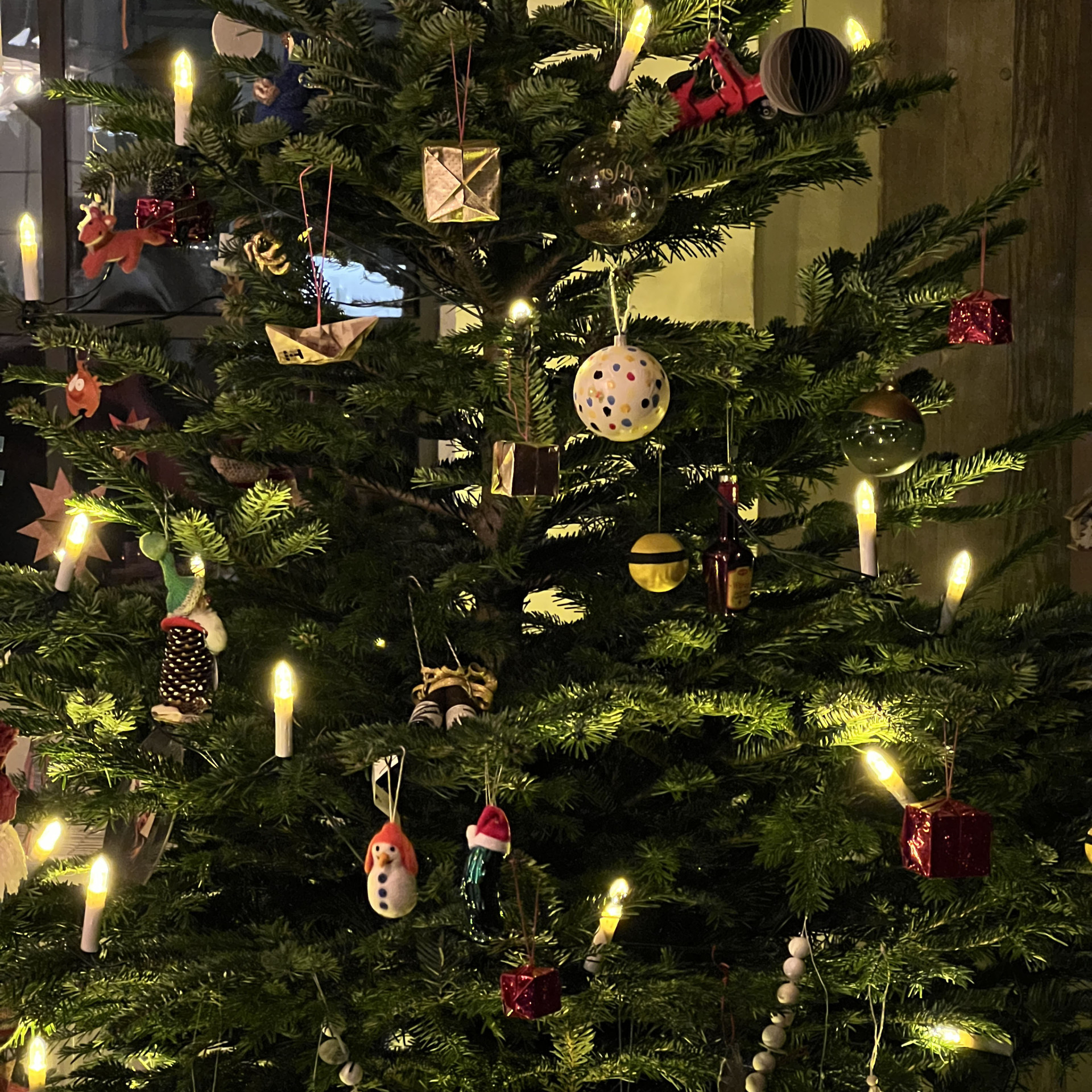 Ein festlich geschmückter Weihnachtsbaum, leuchtend mit Kerzen und bunten Ornamenten.
