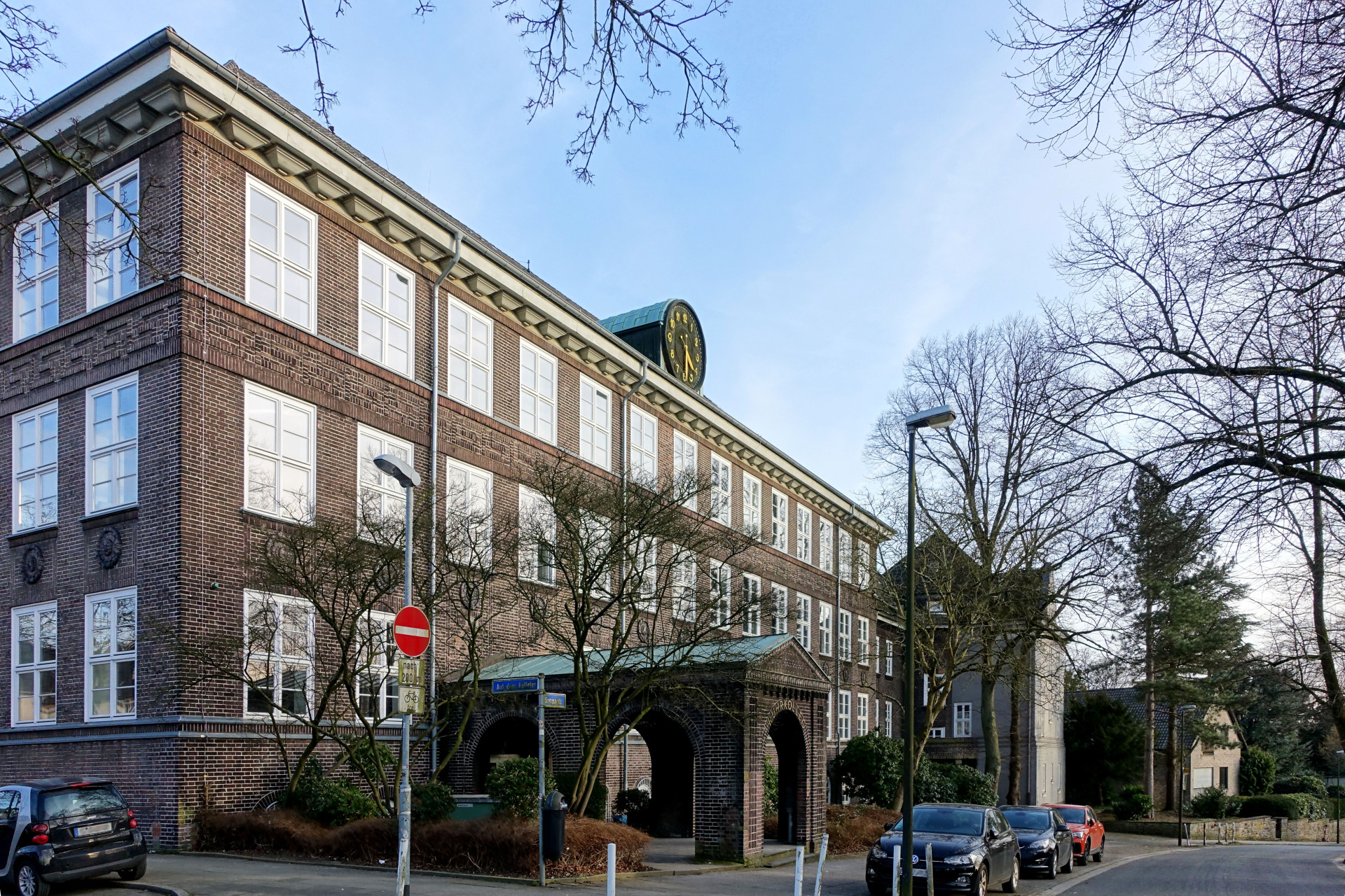 Historisches Gebäude mit grüner Uhr, umgeben von Bäumen und parkenden Autos unter blauem Himmel.
