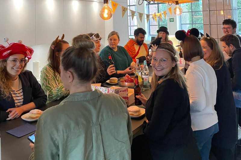 Menschen in Kostümen feiern in einer modernen Küche, Essen und Getränke stehen bereit.