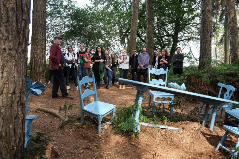 Außenperspektive zeigt Mitarbeitende des Büros, die im Wald vor blauen Tischen und Stühlen stehen.