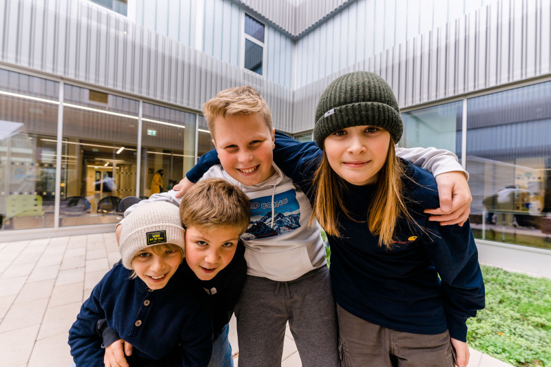 Außenperspektive mit vier Schülern die Arm in Arm im Innenhof der Schule stehen.