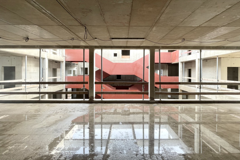 Innenperspektive zeigt den fertiggestellten Rohbau der Schule und den Blick auf die Treppe mit rotem Geländer.