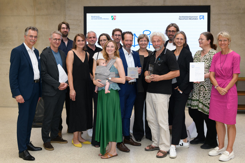 Gruppierung von Preisträger*innen beim Schulbaupreis NRW 2023, alle lächelnd und stolz, in festlicher Atmosphäre.