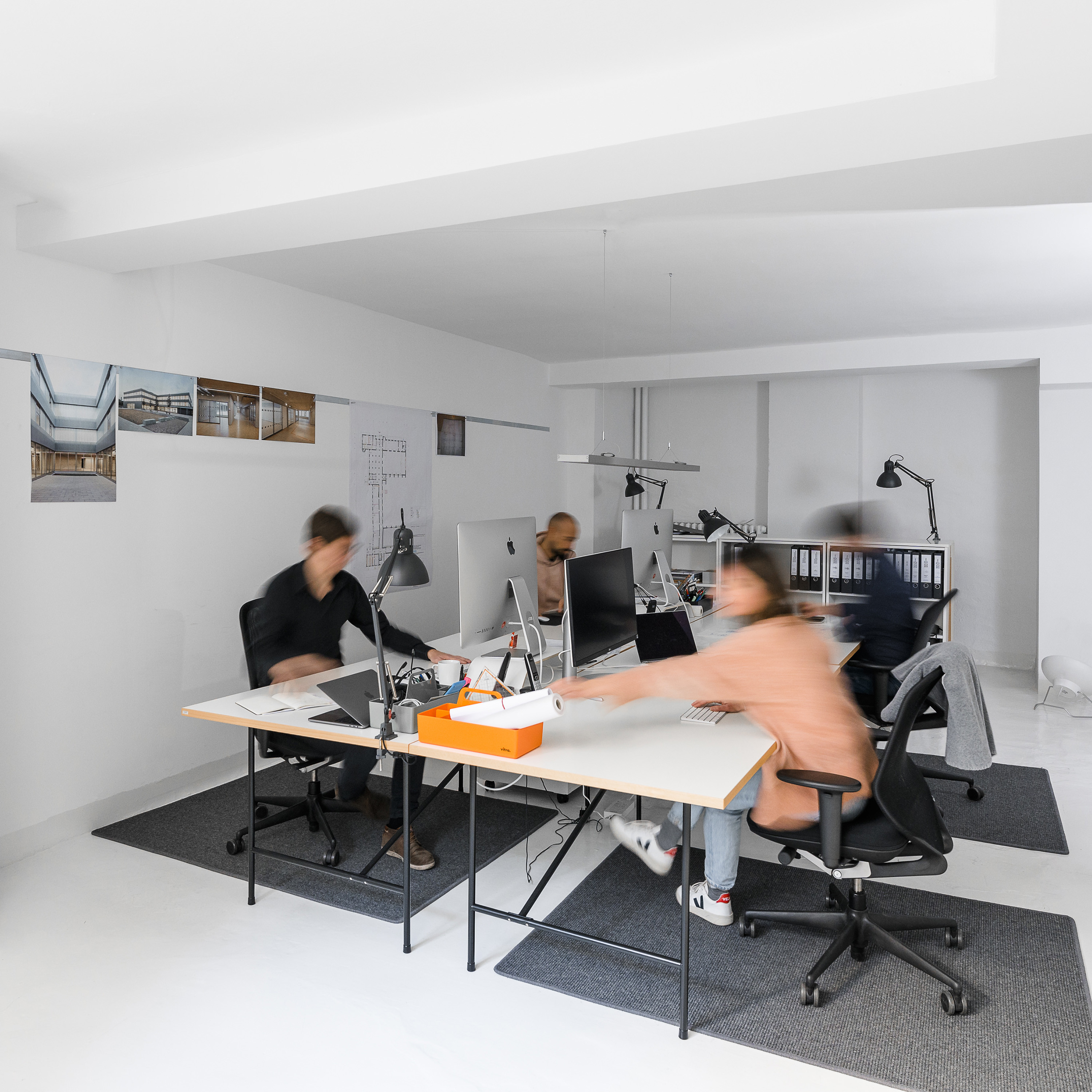 Innenperspektive zeigt arbeitende Mitarbeitende an ihrem Arbeitsplatz in einem weißen Büro.