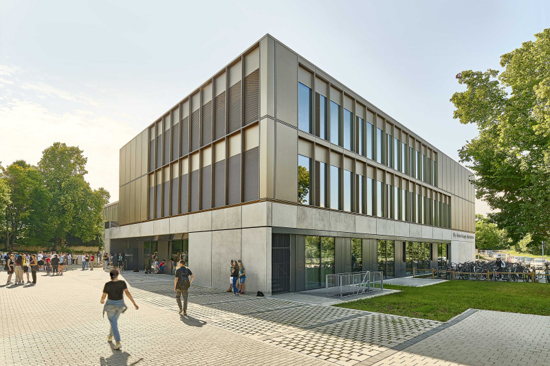 Außenperspektive von der dreigeschossigen Schule mit einem bespielten Schulhof im Hintergrund.