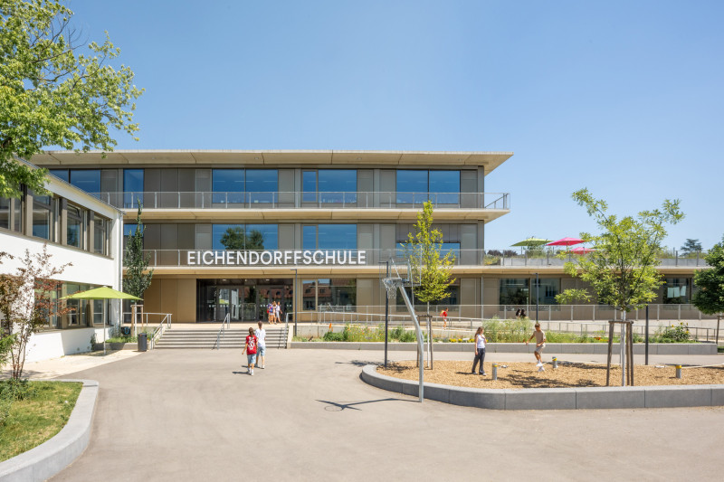 Moderne Eichendorffschule mit flacher Fassade, umgeben von Bäumen und spielenden Kindern.