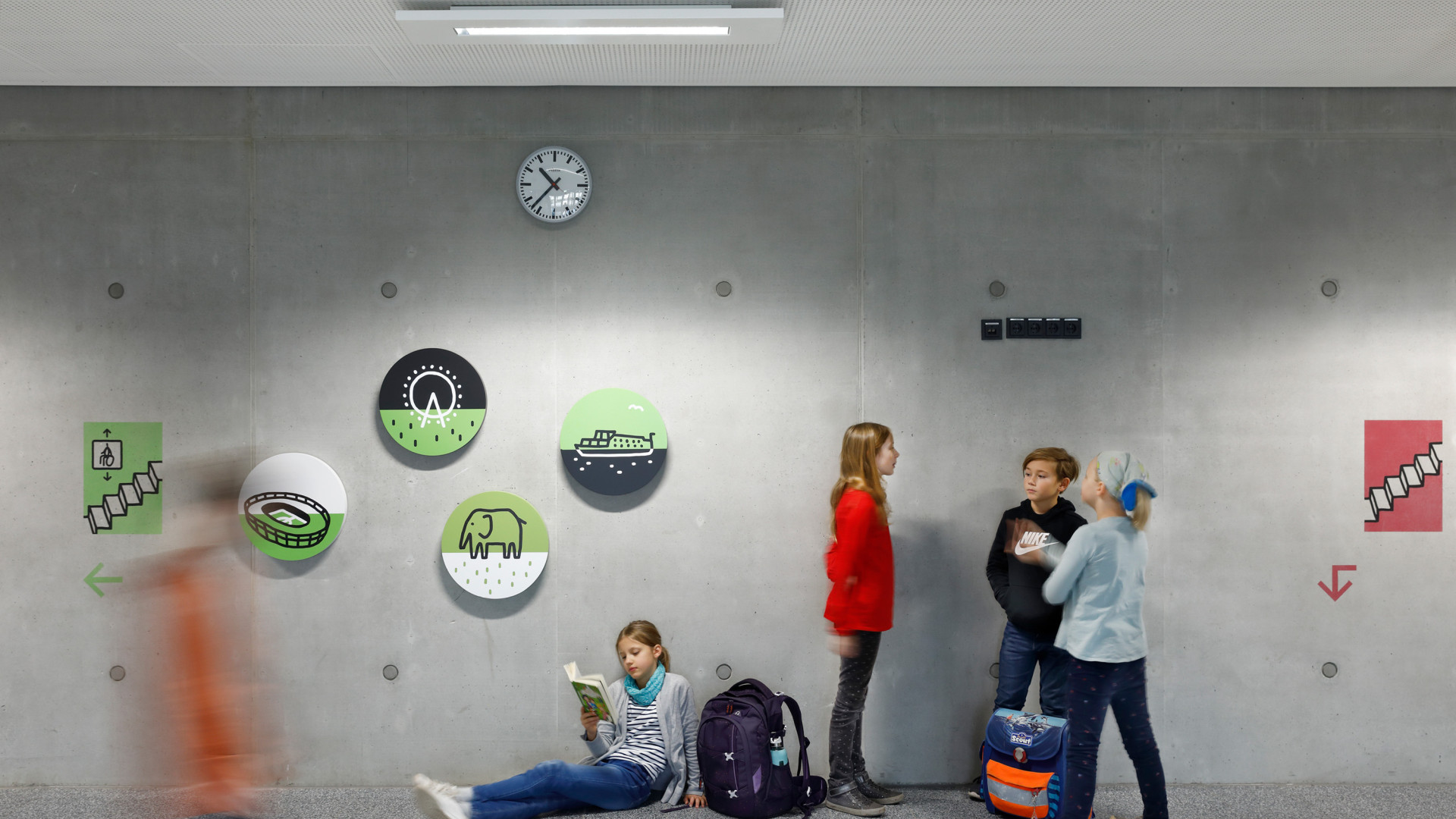 Schülerinnen und Schüler in einem modernen Schulflur mit Wandgrafiken und angedeuteter Bewegung.