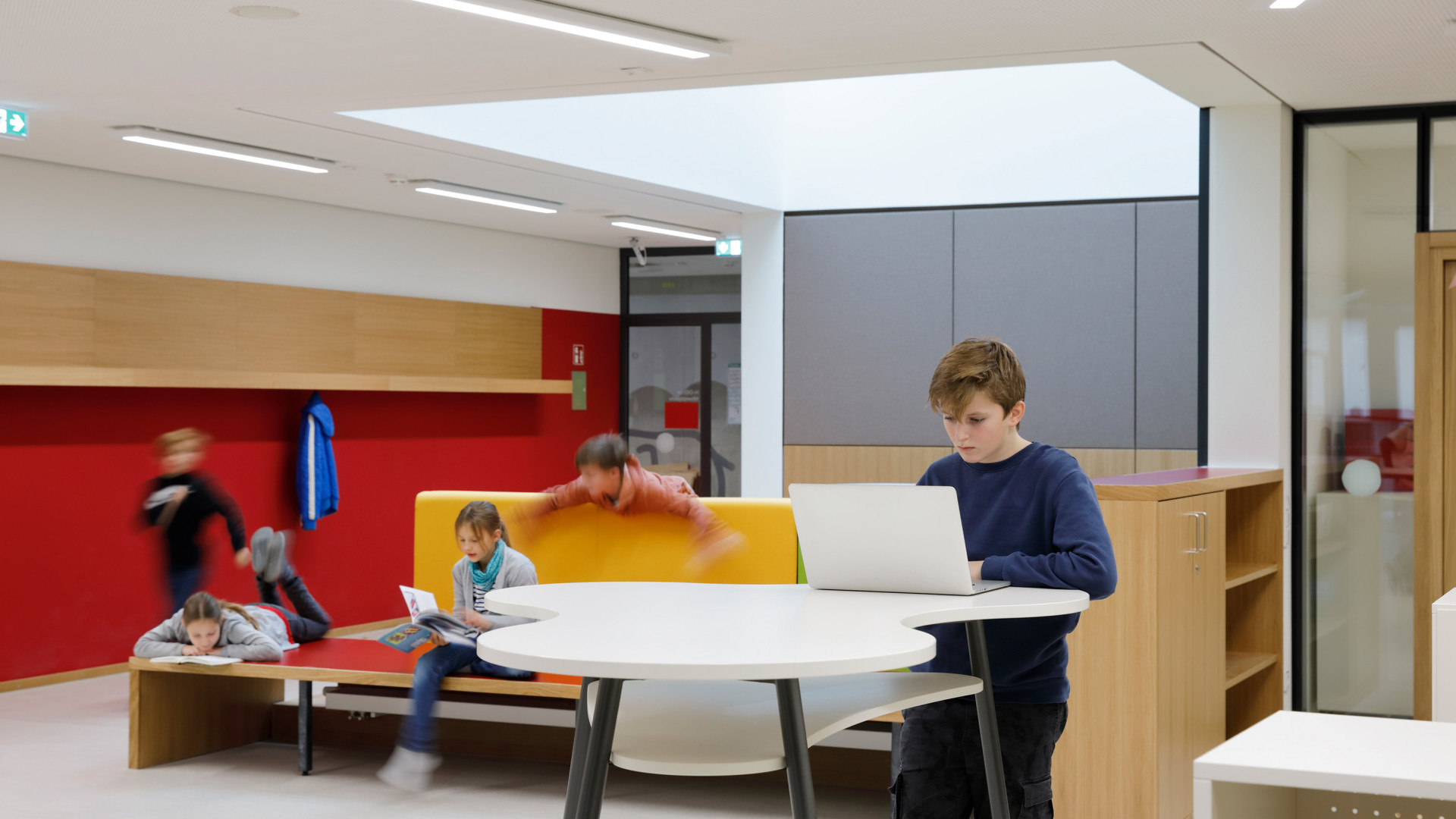 Kinder lernen und spielen in einem modernen Raum mit Sitzmöglichkeiten und einem großen Tisch.