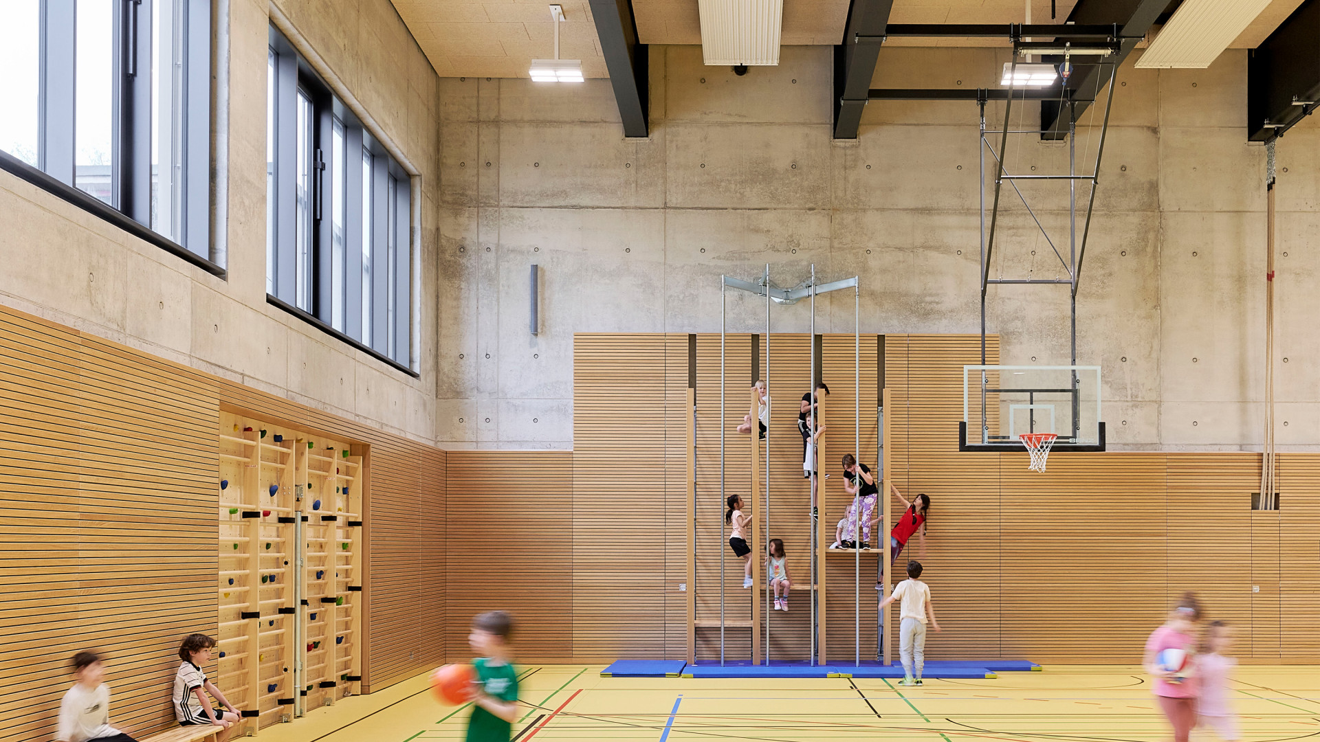 Ein übersichtlicher Sportraum mit Kindern beim Spiel und Klettern an einer Wand.