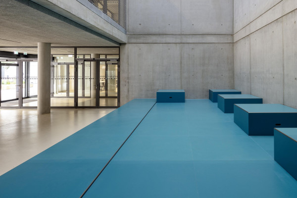 Innenperspektive zeigt das Foyer mit einem blauen Podest im Atrium der Schule.