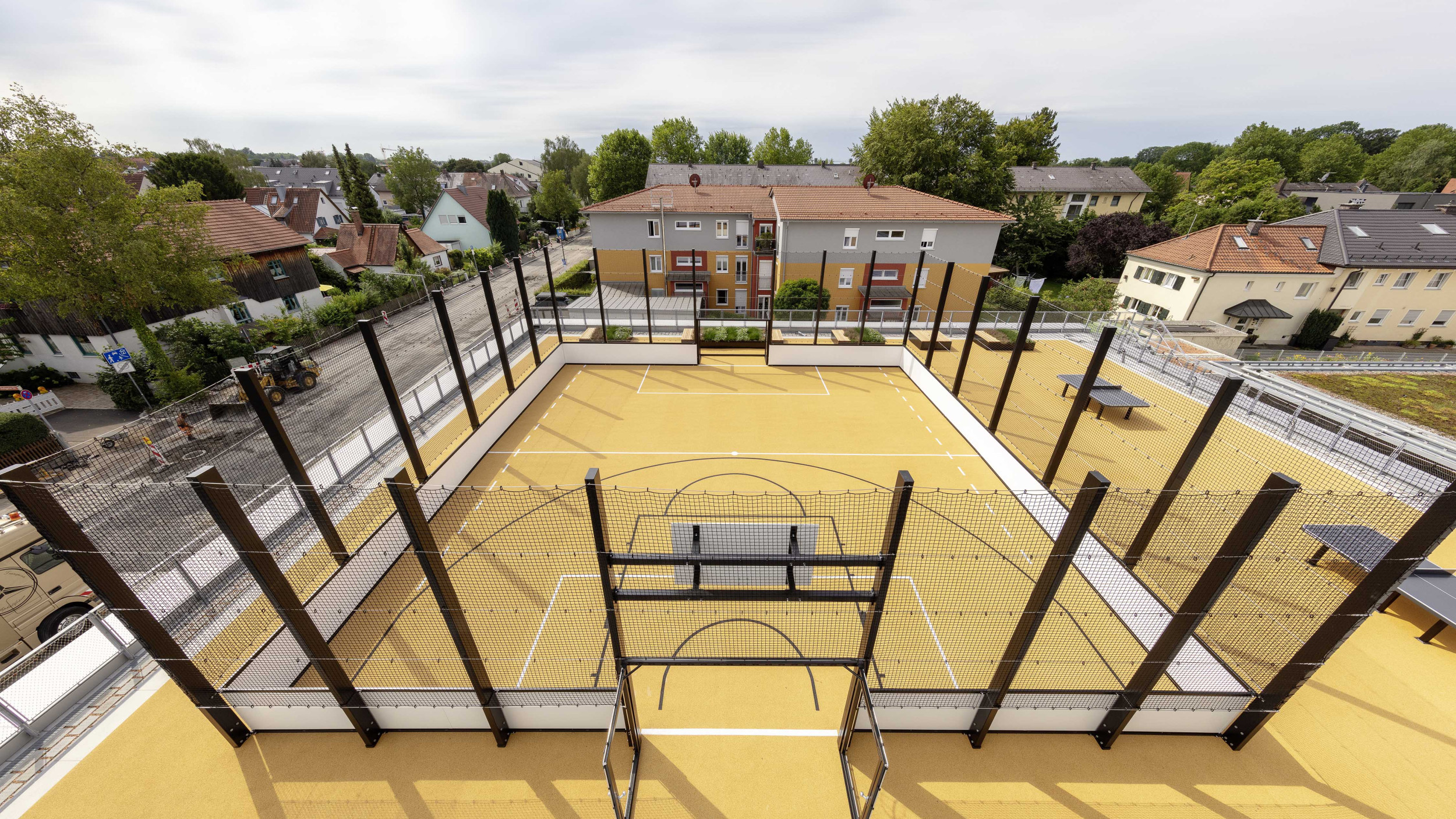 Außenperspektive von einem Sportcourt mit gelbem Boden auf dem Dach der Sporthalle.