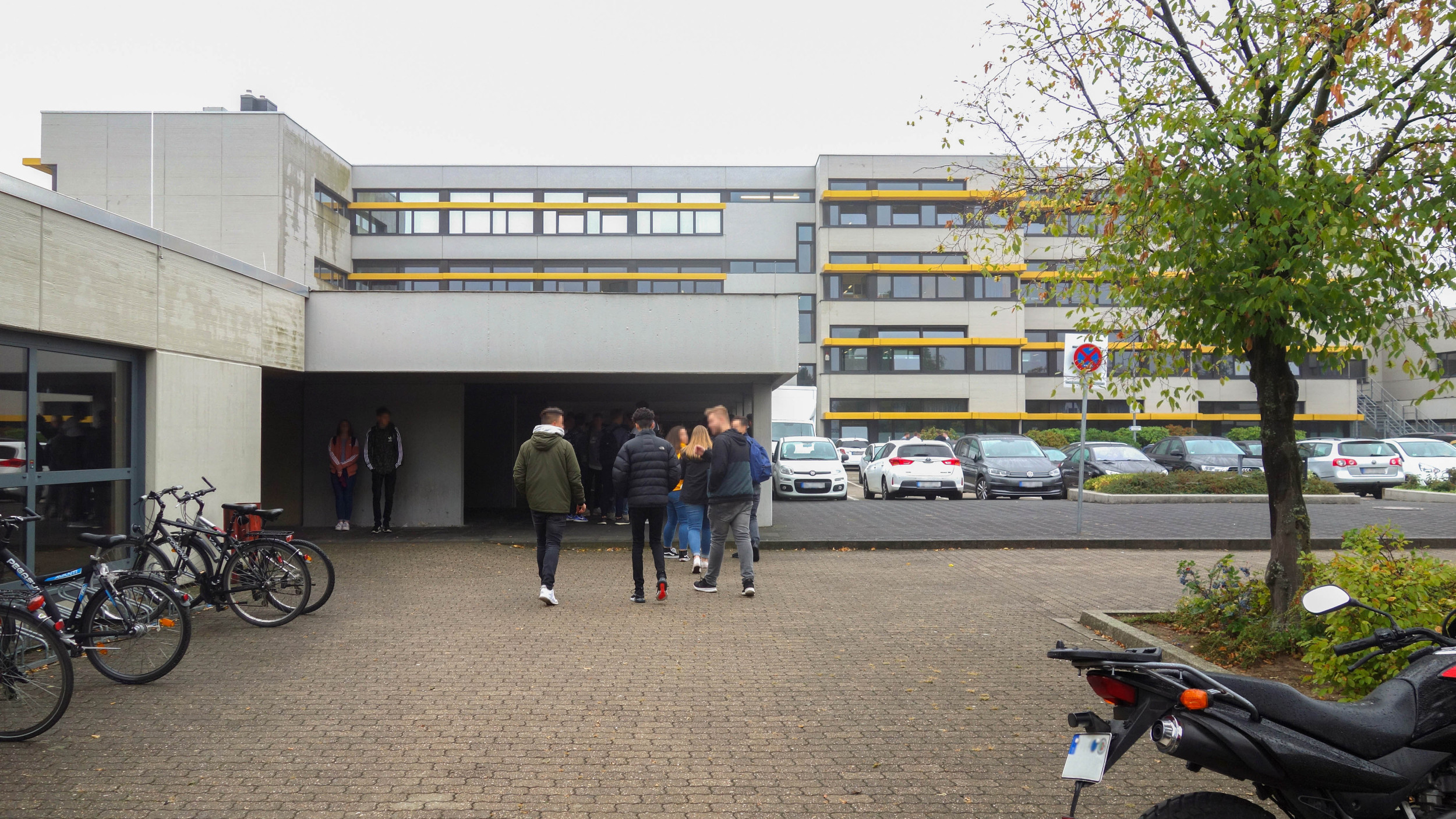 Außenperspektive zeigt eine Gruppe von Schüler:innen, die zum Haupteingang der Schule gehen.