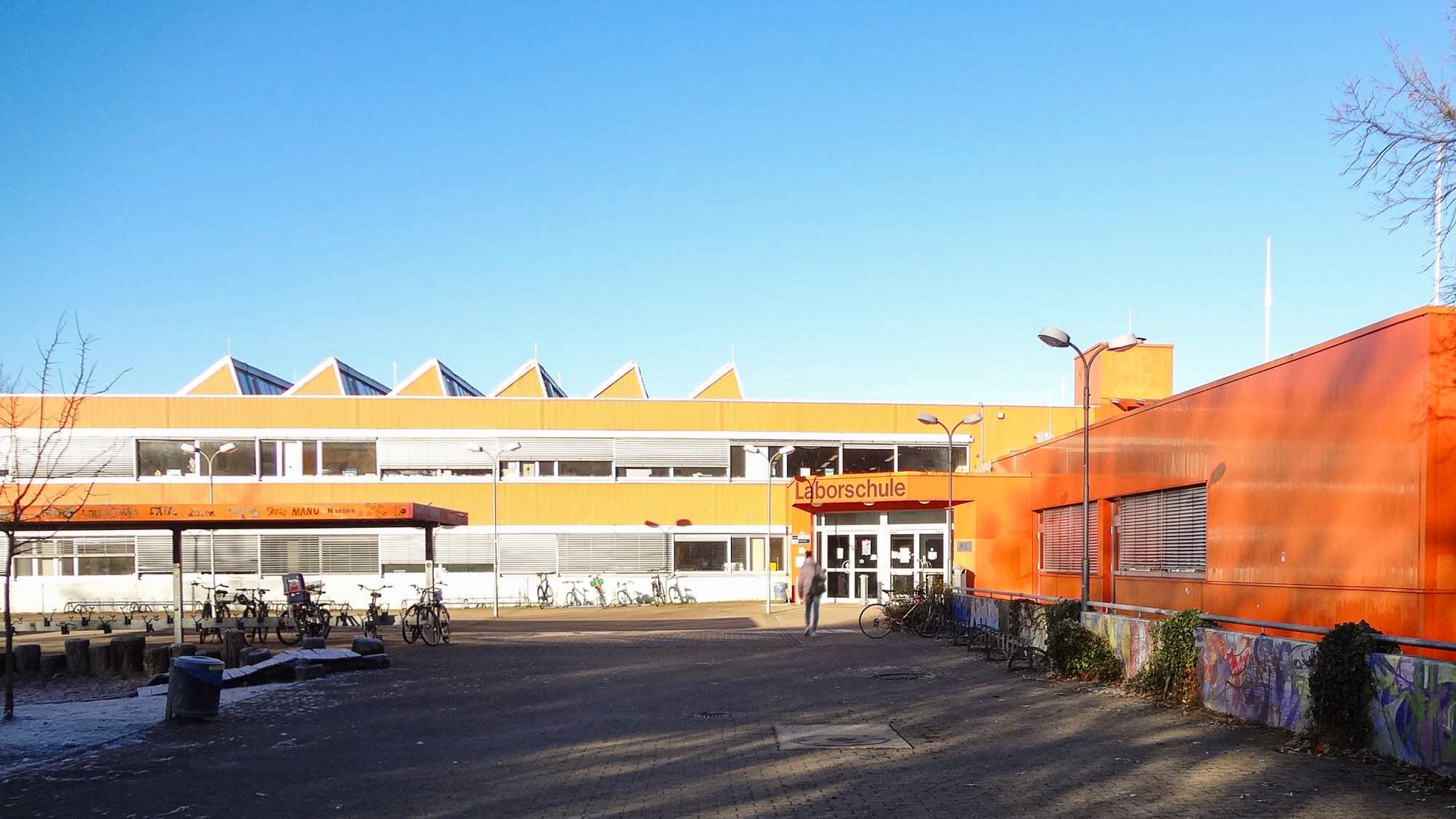 Außenperspektive der zweigeschossigen orangen Laborschule mit der Haupterschließung im Vordergrund.