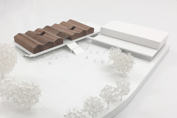 Perspektive zeigt das braune, aus Holz gebaute Schulgebäude in einem weißen städtebaulichen Modell.